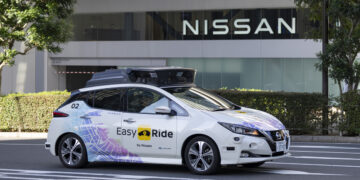 Image of a Nissan vehicle demonstrating autonomous driving capabilities on a busy public road, equipped with advanced sensors and technology.